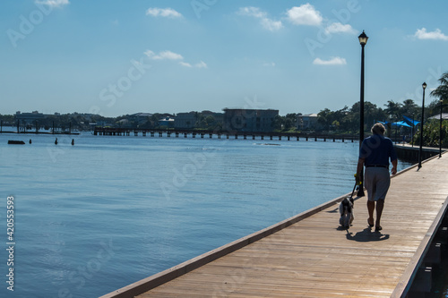 A lone person walks their dog along the St. Lucie Riverwalk, Downtown historic Stuart, Florida. Calm blue water, sunny skies, healthy lifestyle