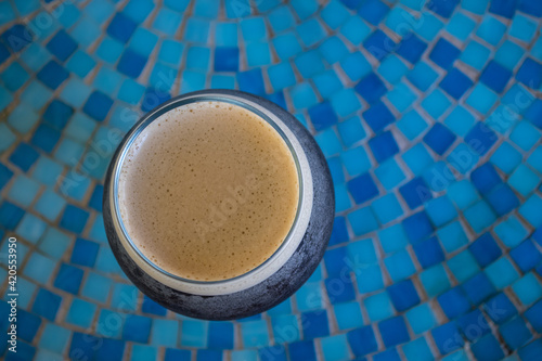 Round glass of cold brewed coffee with foam top sitting on a blue mosaic tiled table at an outdoor cafe.