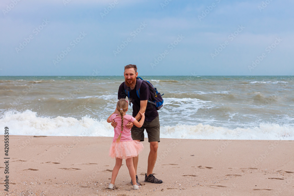 Father holds his cute daughter in arms, circles around himself, play and have fun together on sea beach. Little flying girl smiling hugging with dad outdoor. Loving child and daddy.Father's Day family Father holds his cute daughter in arms, circles around himself, play and have fun together on sea beach. Little flying girl smiling hugging with dad outdoor. Loving child and daddy.Father's Day family