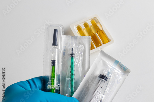 A hand in a medical glove holders syringes, ampoules in the background.