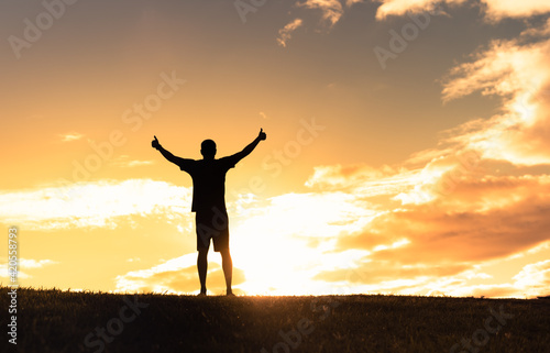 Happy young man feeling free putting arms up to the sunset sky feeling good. 