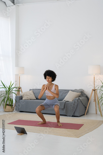 Girl goes in for sports at home, does squats with an elastic band