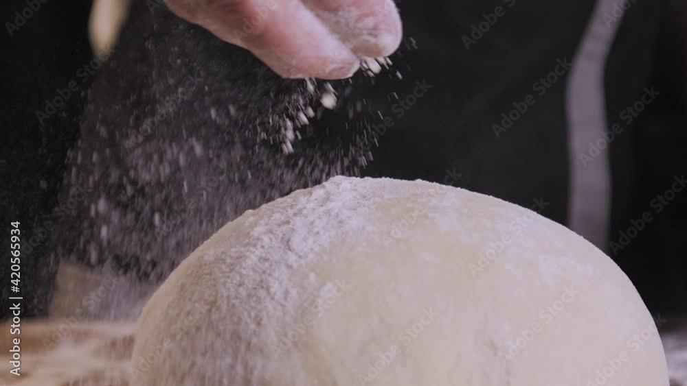 Close-up of baker pours flour on dough. Action. Baker sprinkles pinch of flour on baking. Professional Baker and baking cooking with love Close-up of baker pours flour on dough. Action. Baker sprinkles pinch of flour on baking. Professional Baker and baking cooking with love