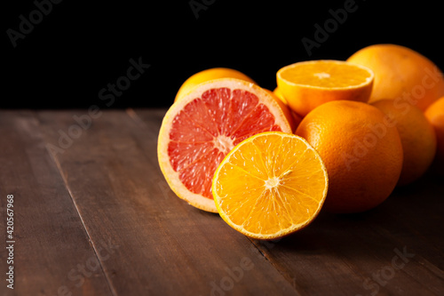 ripe orange and grapefruit slices and several whole oranges on brown rustic wooden table with black background