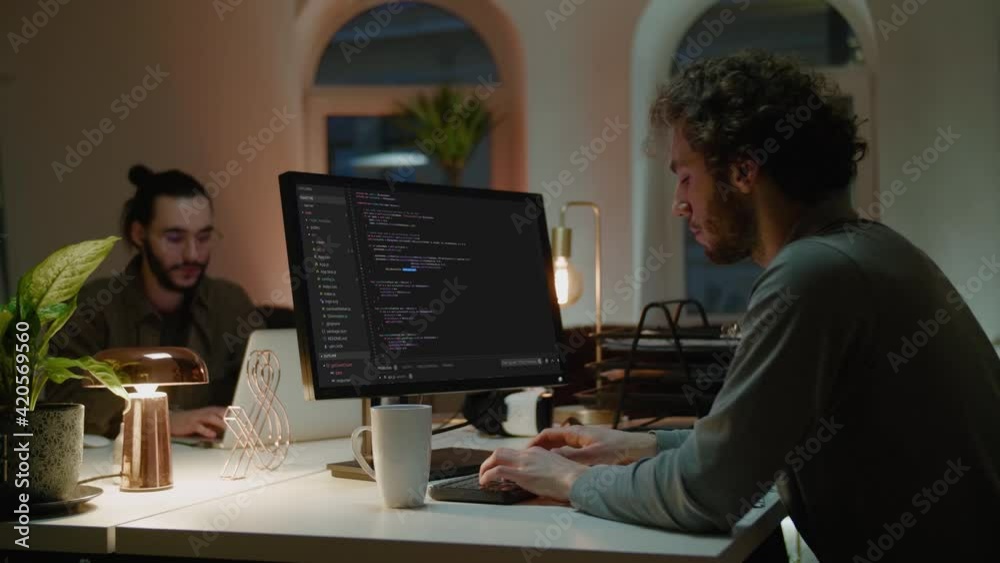 Programmer writes code on computer at table near colleague