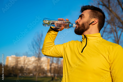 Waist shot of man athlete drinking water from sports bottle, having yellow shirt and ear buds