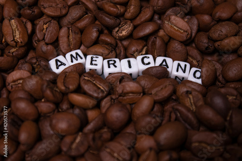 close up of Freshly roasted coffee beans near word AMERICANO written with little white cubes. top view