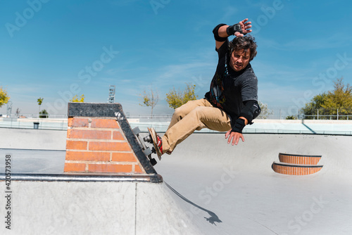 Front view of mid aged man skateboarder in his forties performing stunt on ramp at skate park with safety helmet