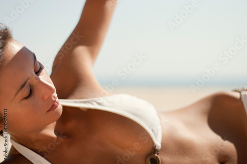 Young woman portrait laying on the sand for a tan at the beach photo