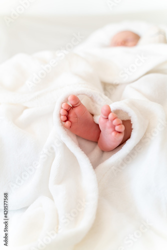 Mother's/Father's loving hand holding tiny, cute, bare feet of a little caucasian newborn baby girl/boy. Baby lying on a white soft and cosy blanket, sleeping. Symbol of love, happiness of a family  