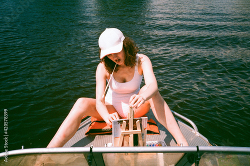 Girl in white swimsuit and hat painting in a boat