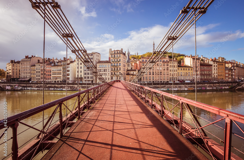 Naklejka premium Cette passerelle relie le quartier Saint Paul au quartier Saint Vincent à Lyon. Elle est peinte en rouge et est suspendue par des câbles à des piliers en pierre.