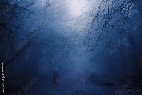 Man walking through the deep blue dark forest. Early morning, winter forest in England.