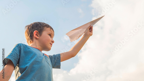 Happy child playing with paper airplane against the sky. A boy with paper airplane © spyrakot