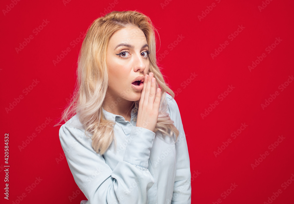 Young woman holding hand near mouth and telling secret, isolated on red background. Gossip concept Young woman holding hand near mouth and telling secret, isolated on red background. Gossip concept