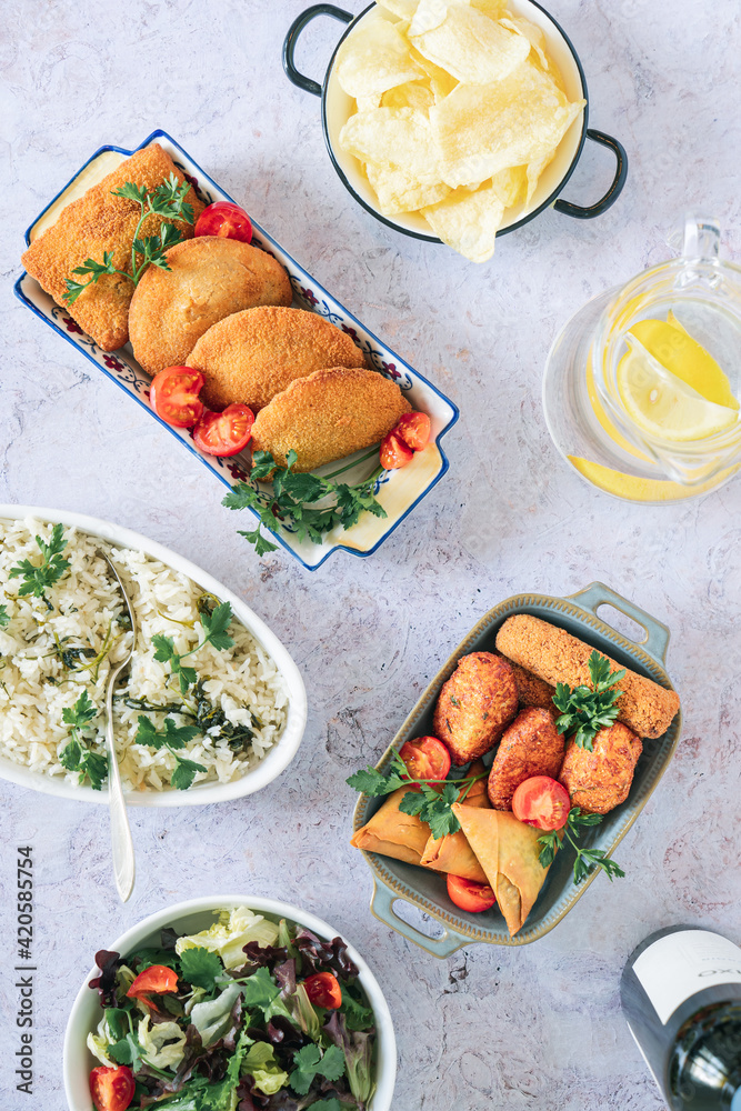 Fototapeta premium Traditional Portuguese fried snacks: cod fish cakes, rissóis, croquettes and samosas with parsley rice, salad, water and wine.