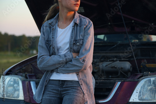 Crop woman leaning on broken vehicle in countryside