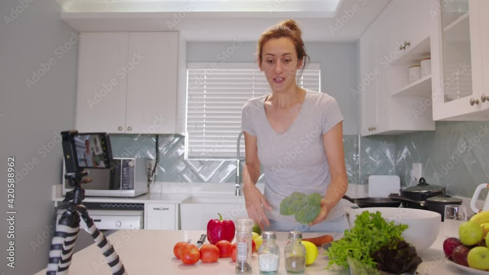 Adorable woman talking recording cooking video at kitchen interior. Beautiful young female blogger preparing healthy food use fresh organic vegetable. Adorable woman talking recording cooking video at kitchen interior. Beautiful young female blogger preparing healthy food use fresh organic vegetable.