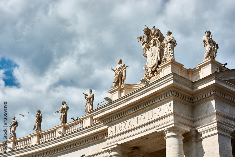 A view of sculptures on top of the Tuscan Colonnades and blue cloudy sky at St. Peter's Square in the Vatican city in Rome, Italy.