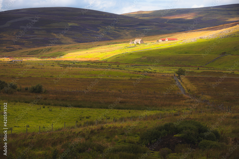 Dramatic dappled light over rural countryside landscape and old farmhouse in the Cairngorms National Park, Scottish Highlands, Scotland.
