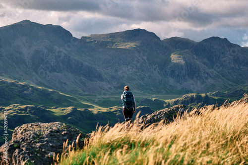 Female walker on Hard Knott looking towards Sca Fell at sunset. Lake District, Cumbria, UK. photo