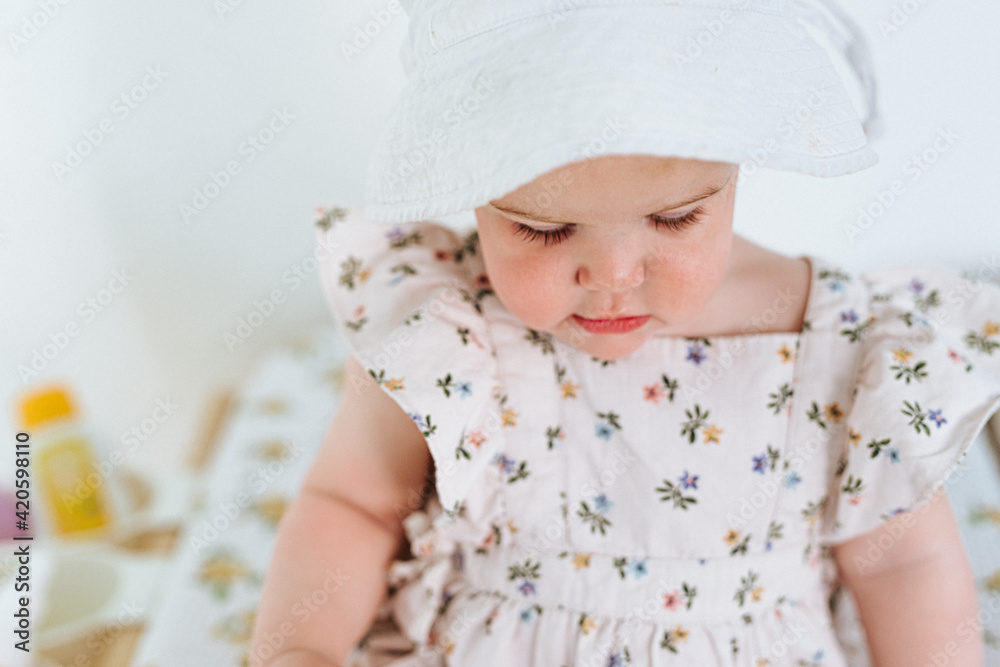 close up of little girl on changing table wearing a sunhat and dress with flowers close up of little girl on changing table wearing a sunhat and dress with flowers