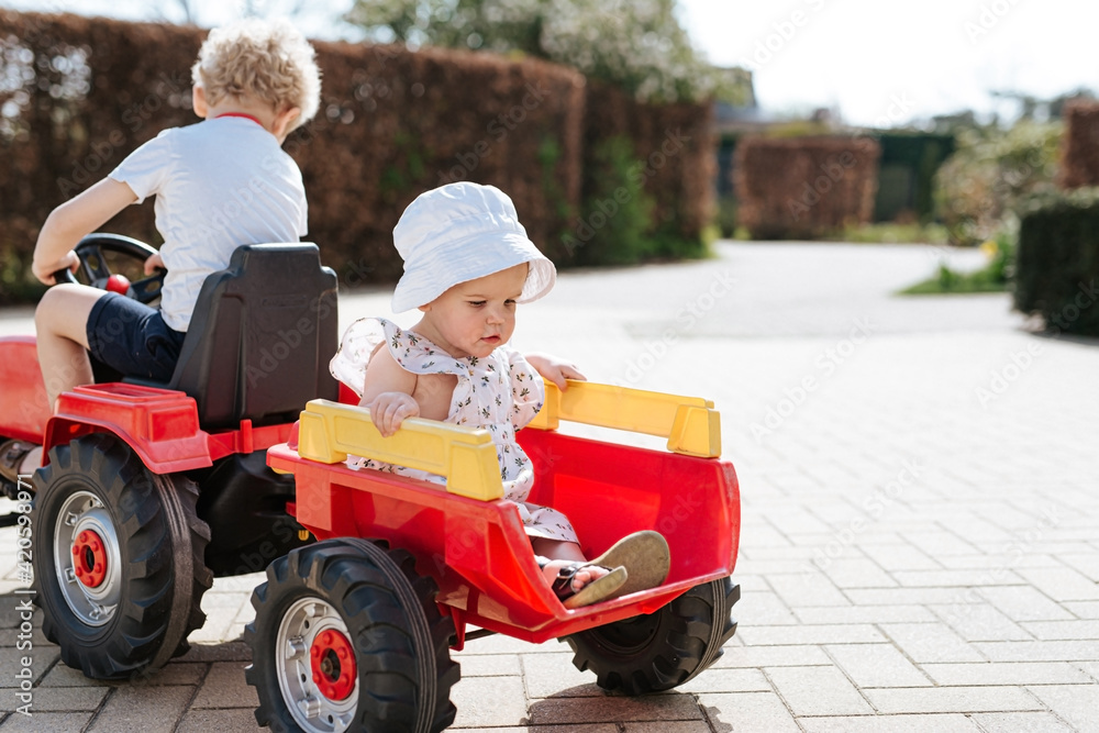 big brother and little sister sitting on a red toy tractor Stock Photo ...