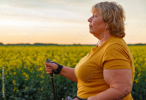 Chubby female walking with sticks against field and sundown sky
