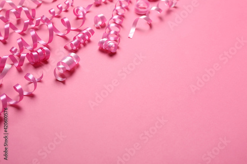 Shiny serpentine streamers on pink background, space for text
