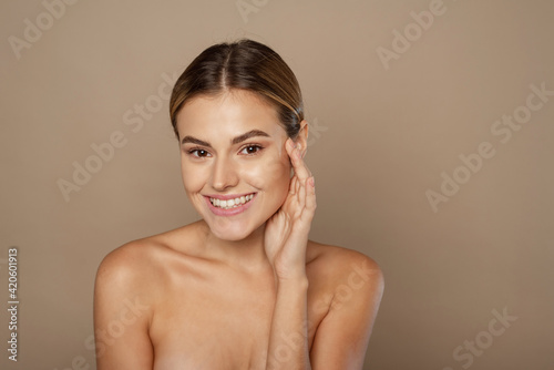 Beauty young woman touches her face with her hands. Young pretty lady with natural makeup on beige background. Beauty, Spa and Skin care concept