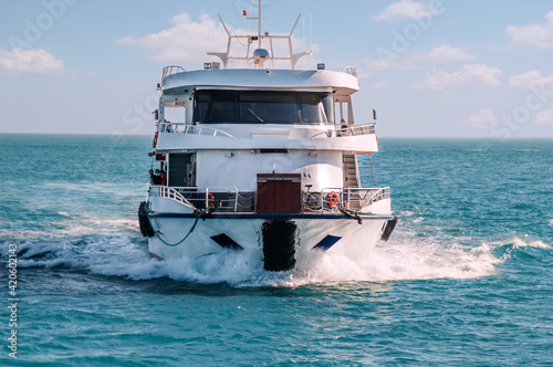 Approaching speedy passenger boat yacht cruising along turquoise sea waters in front of blue sky with white clouds