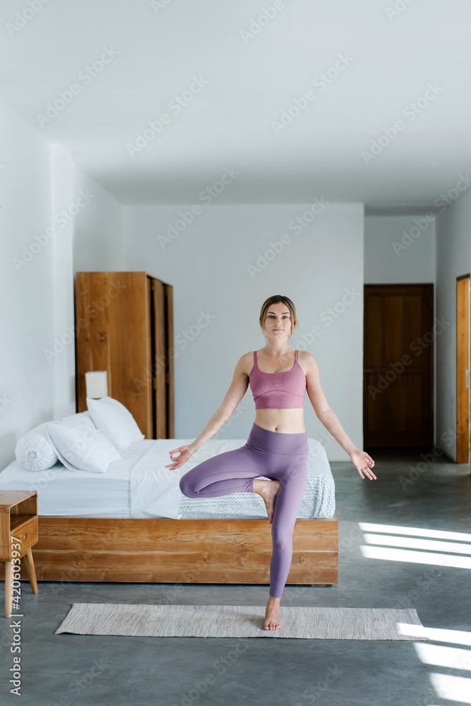 Woman standing near bed in Tree pose Woman standing near bed in Tree pose