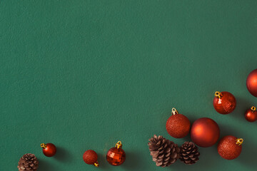 Row of red christmas ball decorations and pine cones on a green background
