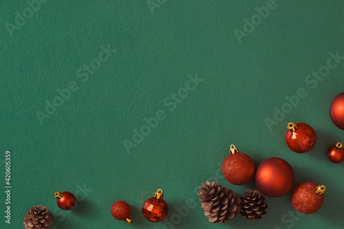 Row of red christmas ball decorations and pine cones on a green background photo