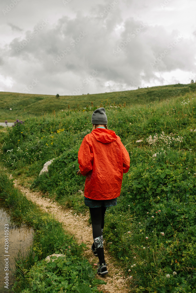 Tourist girl in the bright raincoat walks on the path in the clouds of mountains Tourist girl in the bright raincoat walks on the path in the clouds of mountains
