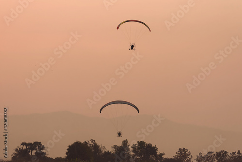 Silhouette of the Paramotor gliding and flying In the air through soft sunlight sky.