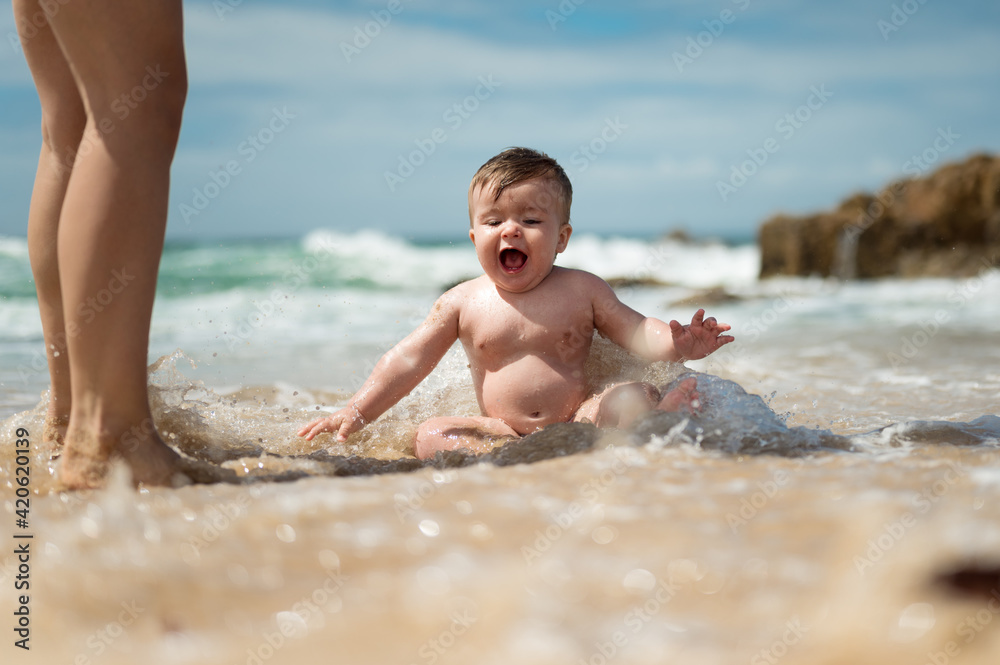 Happy baby playing in waves near mother Happy baby playing in waves near mother