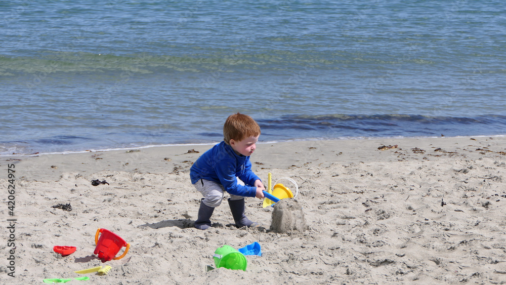 Red headed boy playing with Bucket spade and Digger on a sandy beach Red headed boy playing with Bucket spade and Digger on a sandy beach