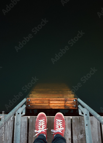 Top view at red sneakers on pier ladder leading down to deep wat