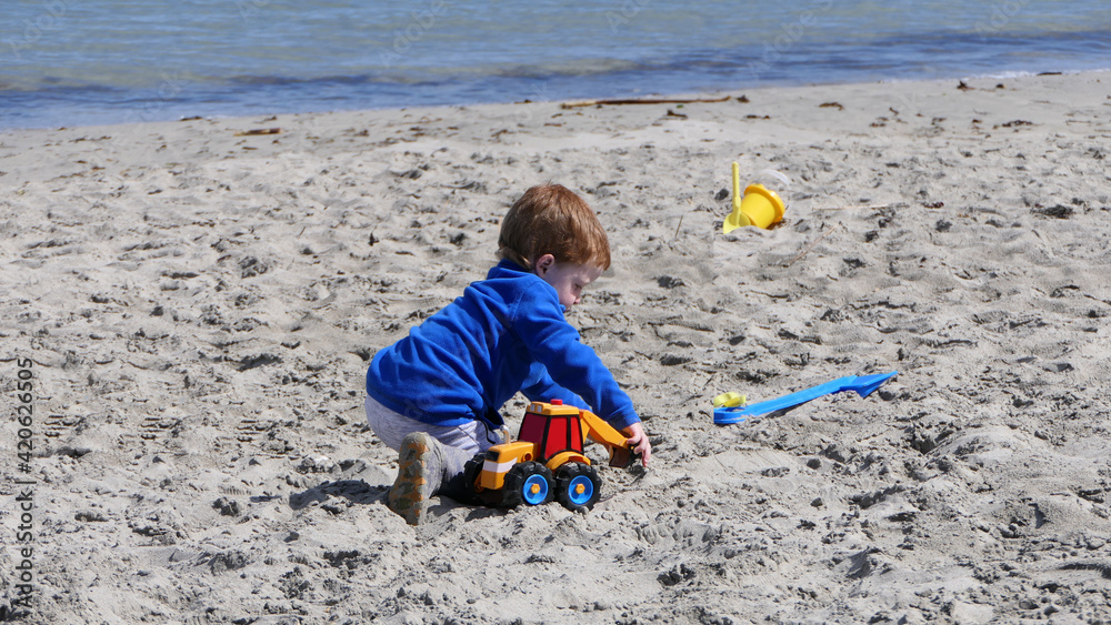 Red headed boy playing with Bucket spade and Digger on a sandy beach Red headed boy playing with Bucket spade and Digger on a sandy beach