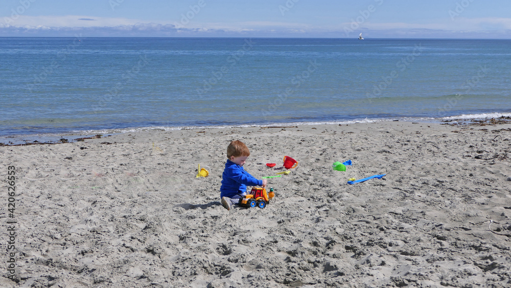 Red headed boy playing with Bucket spade and Digger on a sandy beach Red headed boy playing with Bucket spade and Digger on a sandy beach