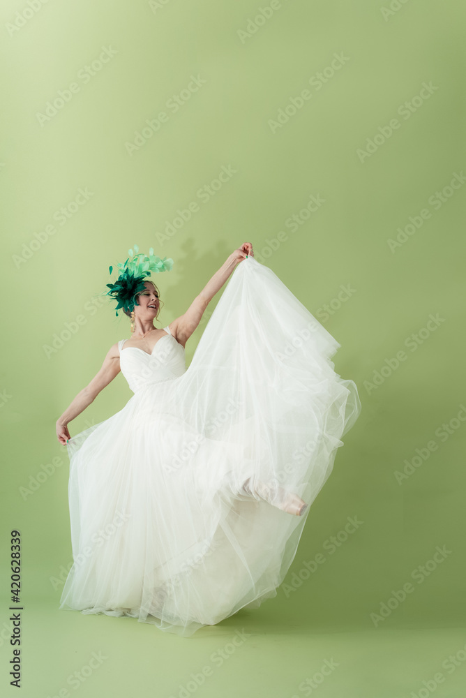 Ballerina bride in tulle wedding gown with green feather headpiece dancing ballet in studio green backdrop Ballerina bride in tulle wedding gown with green feather headpiece dancing ballet in studio green backdrop