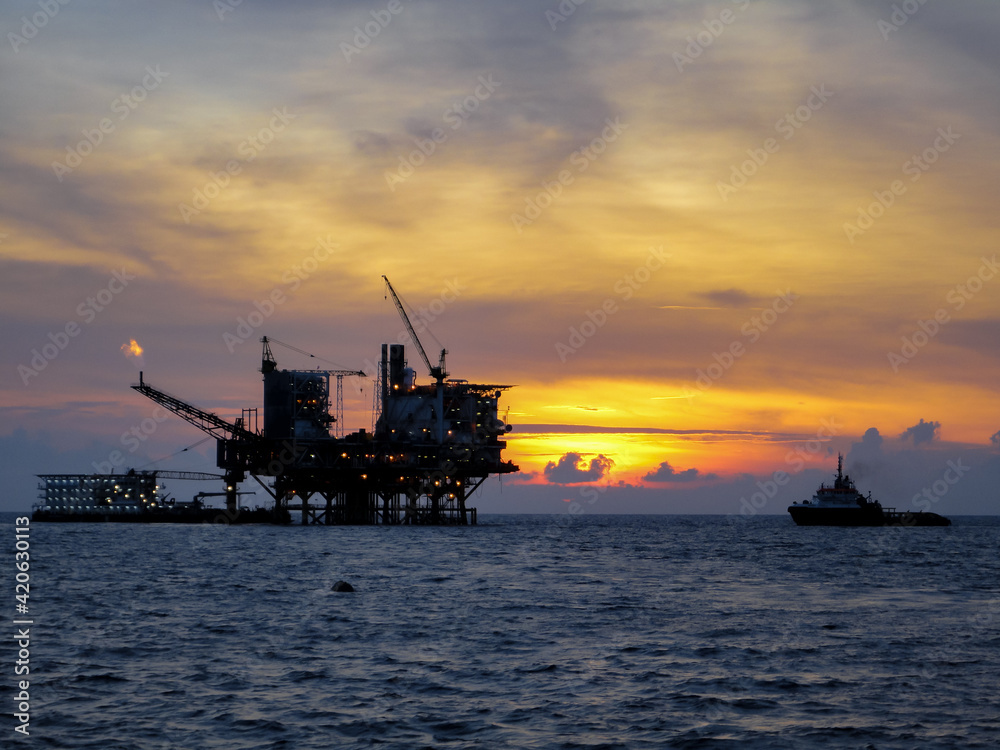 Oil and gas platform in open sea, producing crude oil and gas as a source of energy. Sunset moment in oil field.