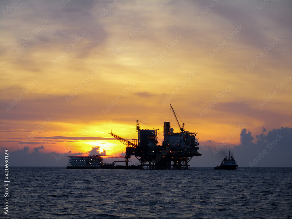 Oil and gas platform in open sea, producing crude oil and gas as a source of energy. Sunset moment in oil field.