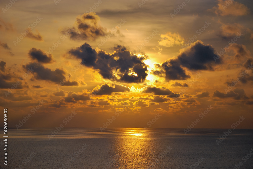 Sunset moment in the middle of the sea, with beautiful clouds covers some parts of the sun creating an amazing ray of light at the horizon. 