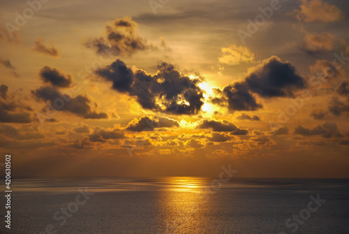 Sunset moment in the middle of the sea, with beautiful clouds covers some parts of the sun creating an amazing ray of light at the horizon. 