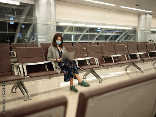 Woman in mask with laptop in empty airport photo