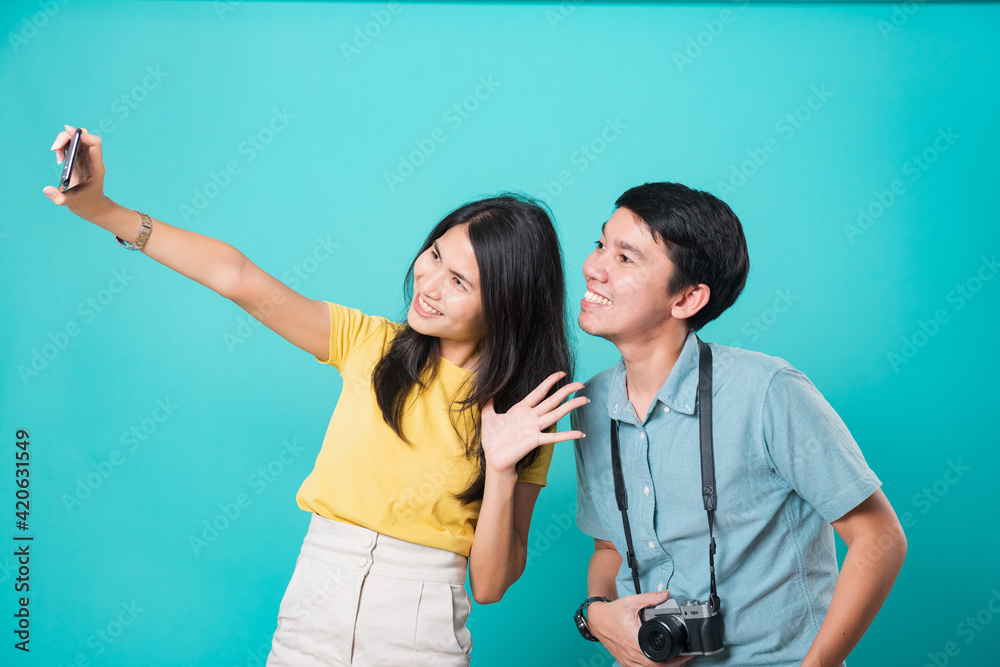 Portrait happy Asian young handsome man, beautiful woman couple smile standing wear shirt, taking selfie photo on a smartphone, studio shot on blue background with copy space Portrait happy Asian young handsome man, beautiful woman couple smile standing wear shirt, taking selfie photo on a smartphone, studio shot on blue background with copy space