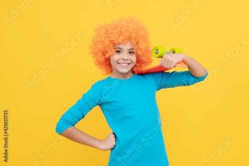 lets have fun. fancy party look. kid in clown wig hold penny board. funny child with fancy hair
