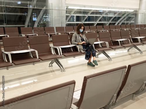 Woman in mask with laptop in empty airport photo